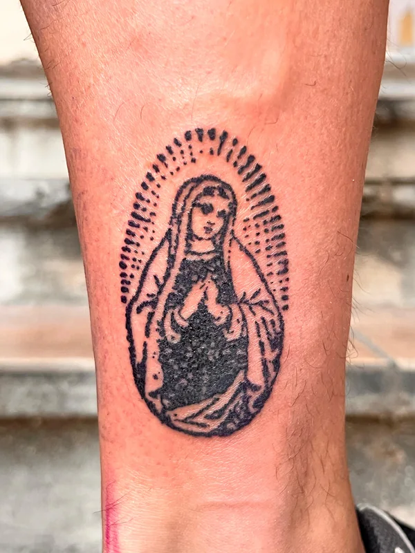 Vierge dans un médaillon rayonnant, tatouée par Inocent Kidd sur une cheville